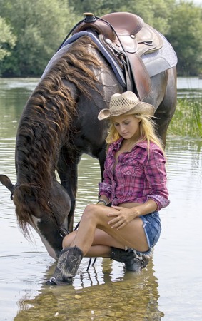 Beautiful blond woman holding brown horse in the waterの写真素材