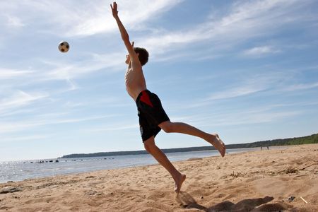 teen boy playing football on a beachの写真素材