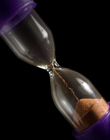 hourglass with last grains of falling sand isolated on black