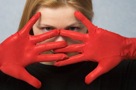 young grey-eyed woman with hands in red gloves in front of her faceの写真素材