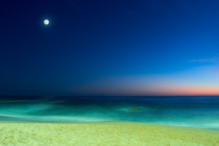 evening seascape with sandy beach, calm ocean and full moon on blue sunset sky の写真素材