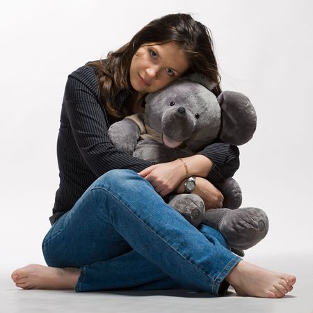 young beautiful woman with long dark hair sitting on the floor with big toy mouse in hands on white backgroundの写真素材