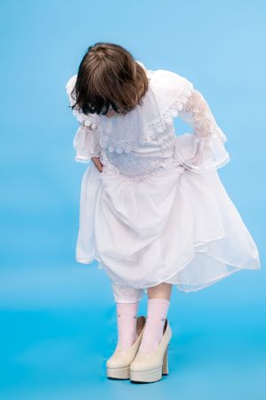 funny little girl in beautiful white dress and in big adult shoes on blue backgroundの写真素材