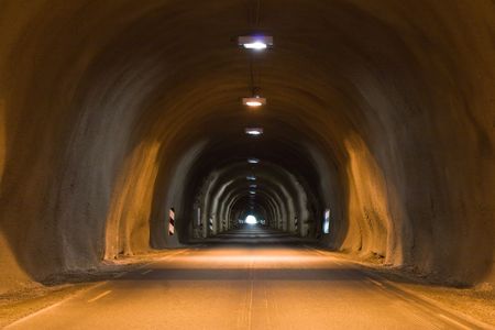 front view of long dark tunnel with bright light at the endの写真素材