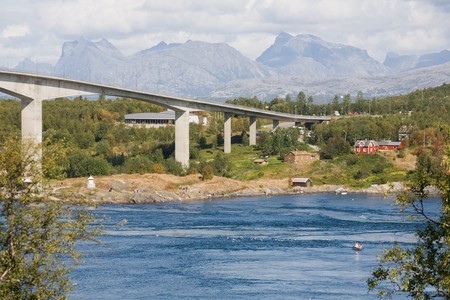modern bridge above the river, trees, mountains, little houses under bridgeの写真素材