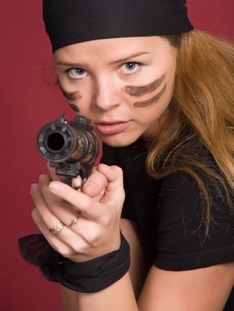 beautiful aggressive girl-pirate close-up directs a pistol on you on red background