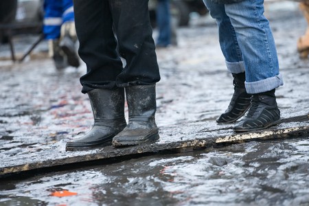 People in rubber boots and in gym shoes stand on a wooden plate in the middle of a puddleの写真素材