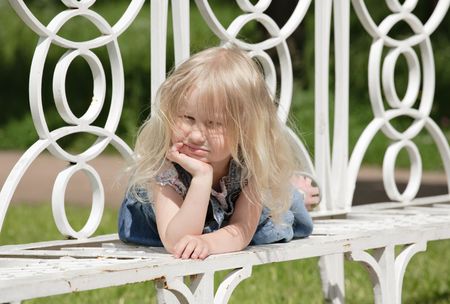 little blonde girl laying on the bench in parkの写真素材