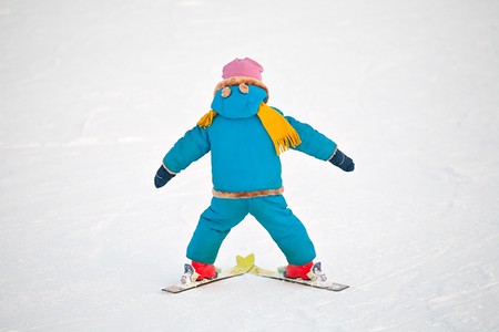 little child doing his first downhill on alpine skis, standing back closeup on snow backgroundの写真素材