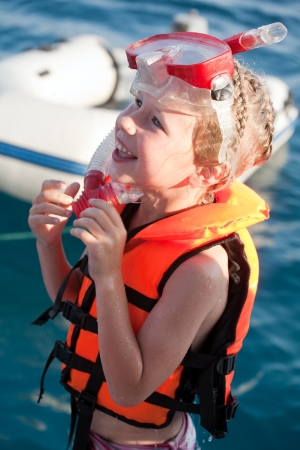 smiling little girl in life jacket and diving mask and snorkel on sea water backgroundの写真素材
