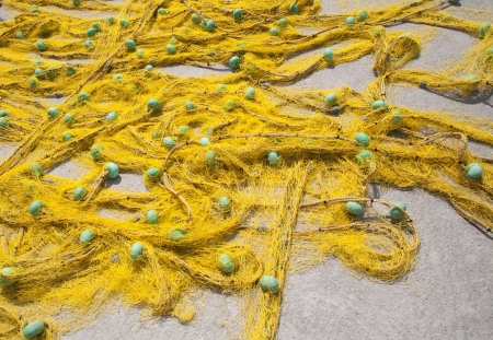 closeup of yellow fishing net with blue float laying on the groundの写真素材