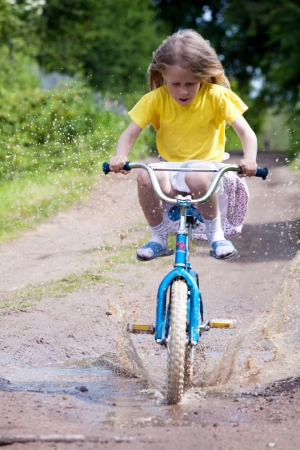 little girl on the bicycle driving through big puddleの写真素材