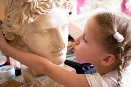little girl kissing the head of ancient Roman statueの写真素材
