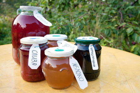 homemade compote and jam pots with Russian labels on the table on orchard background