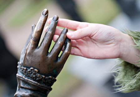 touch closeup of two hands: metal statue and human childの写真素材