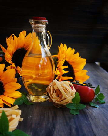 Sunflowers, pasta, tomatoes, basil and a bottle of oil on a wooden backgroundの写真素材