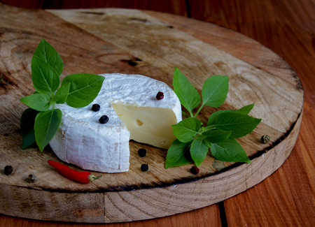 piece of cheese with basil komamber on a wooden board fnd paperの写真素材