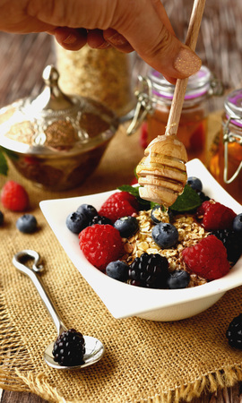 oatmeal with berries and honey in a bowl on a wooden table, selective focusの写真素材