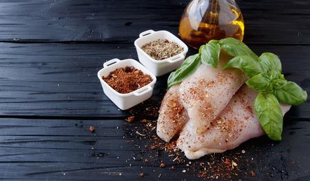raw chicken breasts with herbs spices and vegetables on a black wooden background, selective focusの写真素材