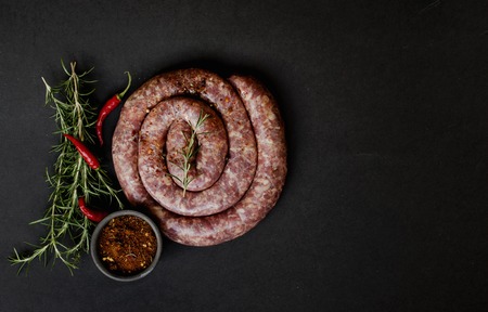raw beef sausages on a cast-iron pan with rosemary and spices on a wooden table, South African boereworsの写真素材