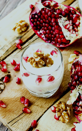 yogurt dessert with walnuts and fresh pomegranate on the wooden table, selective focusの写真素材