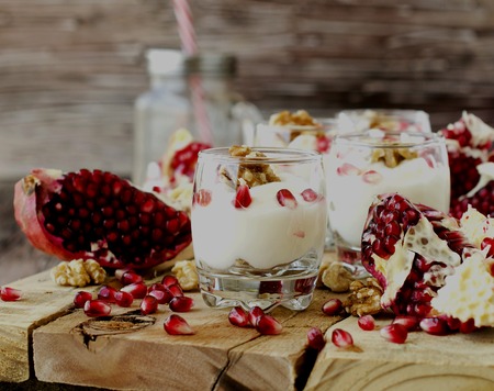 yogurt dessert with walnuts and fresh pomegranate on the wooden table, selective focusの写真素材