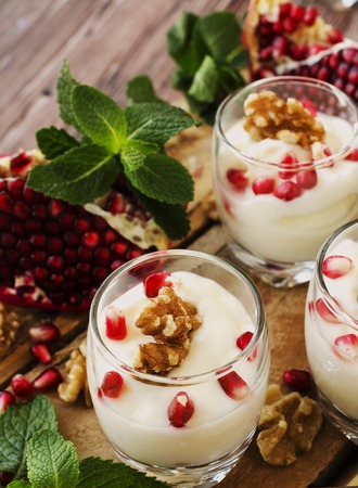 yogurt dessert with walnuts and fresh pomegranate on the wooden table, selective focusの写真素材