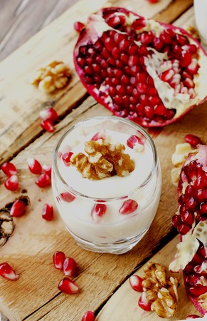 yogurt dessert with walnuts and fresh pomegranate on the wooden table, selective focusの写真素材