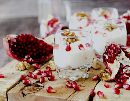 yogurt dessert with walnuts and fresh pomegranate on the wooden table, selective focusの写真素材