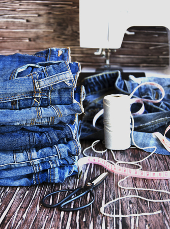 stack of jeans lying on a wooden table, sewing machine and supplies for sewing, selective focus