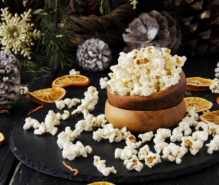 popcorn in a wooden plate on the background of Christmas trees and Christmas decorations, New Year offer, selective focusの写真素材