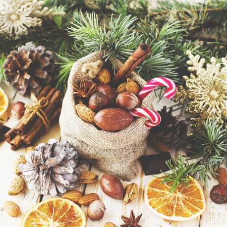 New Year or Christmas composition with walnuts, mulled wine, hazelnuts, pistachios in canvas bags with fir branches and cones. wood background, selective focusの写真素材