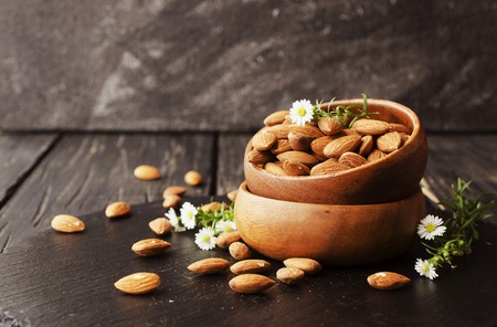 raw almonds in a wooden bowl with flowers, selective focus, space for textの写真素材