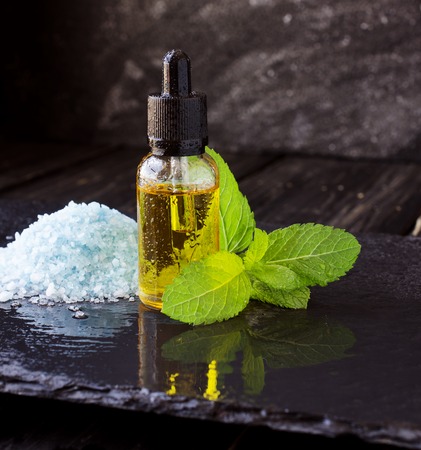jar of menthol oil, a sprig of mint and salt on black stone table for spa, selective focus, space for textの写真素材