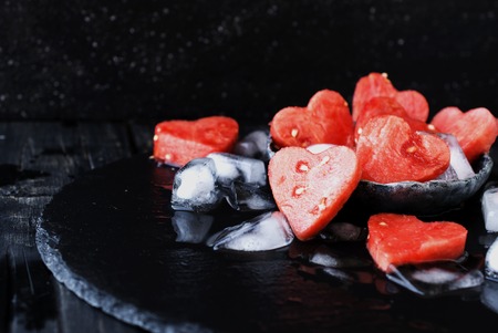 watermelon hearts with ice cubes on black stone background for Valentine's Day, selective focus, space for textの写真素材