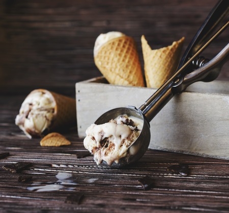 chocolate ice cream in a sugar waffle cones on the wooden background with a spoon, selective focus, space for textの写真素材