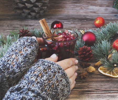 woman's hands holding a cup of mulled wine between Christmas balls with fir branches lying on a wooden table, selective focusの写真素材