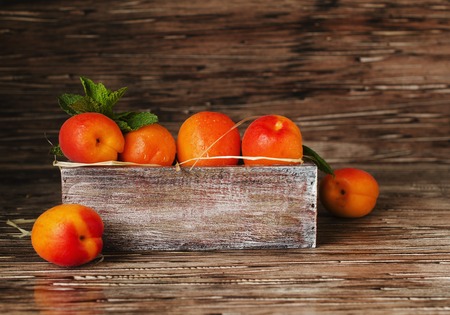 Fresh apricots in a small wooden box and herbs on rustic table, selective focus, top viewの写真素材
