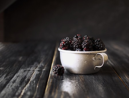 fresh raw ripe blackberries in a metal cup on black wooden table, selective focus, space for textの写真素材