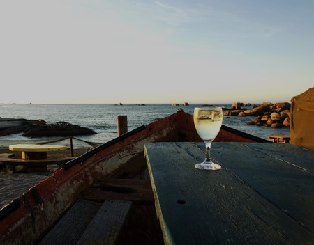 glass of white wine on the old boat table in a cafe on the beach at sunset, selective focusの写真素材