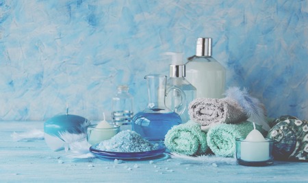 Set for spa with towels, salt and aromatic oils, candles and seashells on a wooden blue background, selective focus, space for textの写真素材