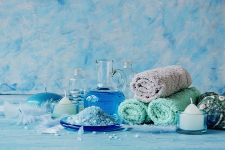 Set for spa with towels, salt and aromatic oils, candles and seashells on a wooden blue background, selective focus, space for textの写真素材