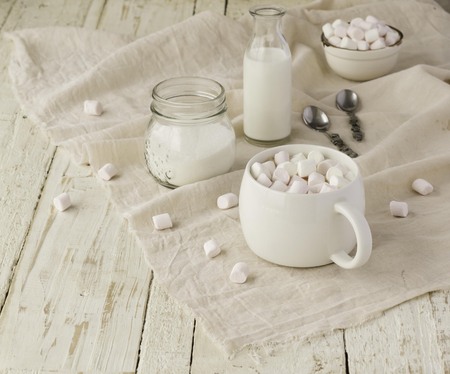 white cup with cocoa and marshmallows on the wooden table with drapes, sugar and milk, selective focusの写真素材
