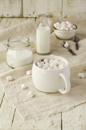 white cup with cocoa and marshmallows on the wooden table with drapes, sugar and milk, selective focusの写真素材