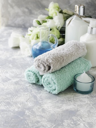 Spa set on a white marble table with a stack of towels, colors, accessories, and bath with sea salt and aromatic oil, selective focusの写真素材
