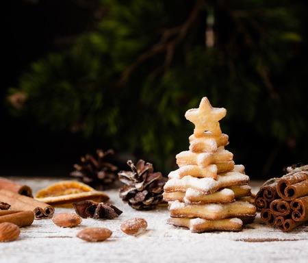 A small Christmas tree of gingerbread biscuit sprouts on a wooden table with cinnamon and nuts,...