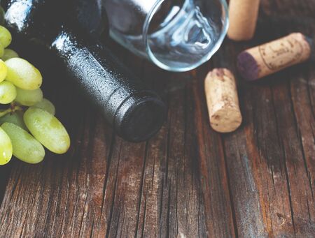 Bottle of red wine with fresh grape and bunch of corks on wooden table, background selective focus -...