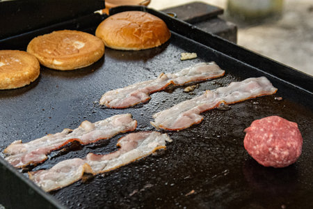 Slices of bacon being grilled on a hot pan with buns