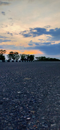 Asphalt road in the evening with trees in the foreground and sunsetの写真素材