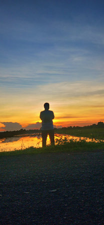 Silhouette of a young man at sunset on the river bankの写真素材